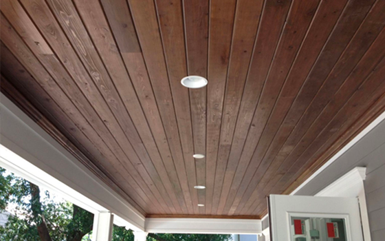 Detail of dark brown wood paneling on porch ceiling with small white lights.